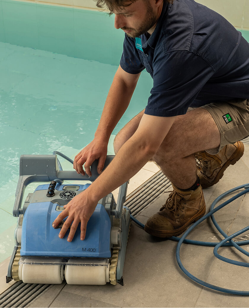 Technician servicing a robotic pool cleaner on the pool edge
